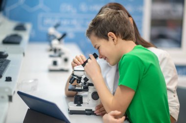 Çocuk mikroskopla bakıcılık öğretmeninin yanına bakıyor.