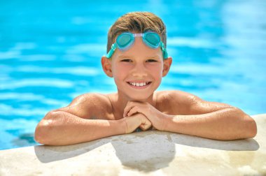 Havuzdan dışarı bakan çocuk kameraya bakıyor.