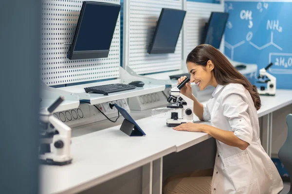Женщина сидит за столом и работает с микроскопом — стоковое фото