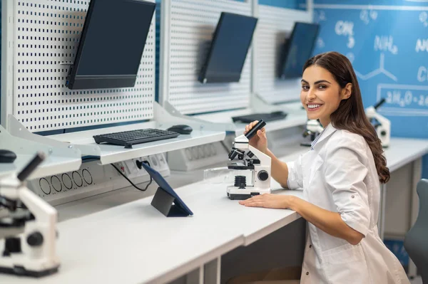 Mulher sentada perto do microscópio olhando para a câmera — Fotografia de Stock