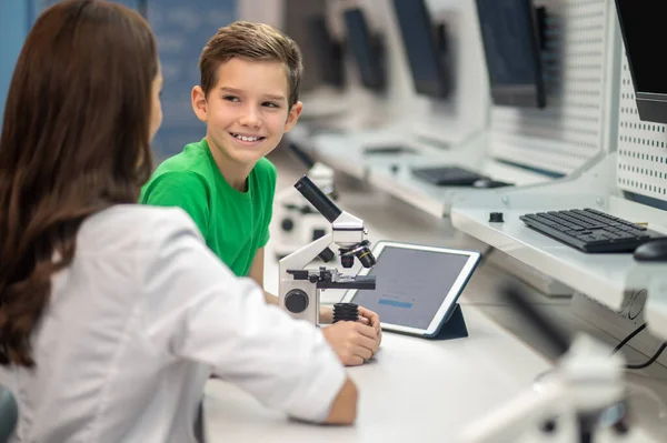 Chłopiec blisko mikroskopu patrząc na nauczyciela — Zdjęcie stockowe