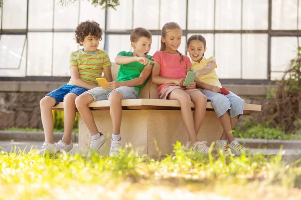 Niños con smartphones sentados en el parque — Foto de Stock