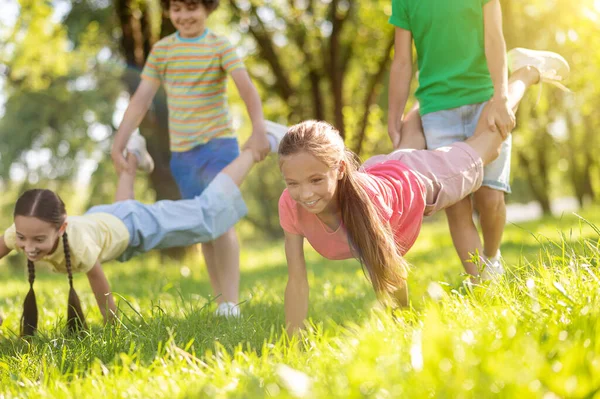 Niños sosteniendo las piernas de las niñas apoyando las manos en la hierba — Foto de Stock