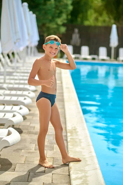 Menino de pé perto da piscina gesticulando ok — Fotografia de Stock