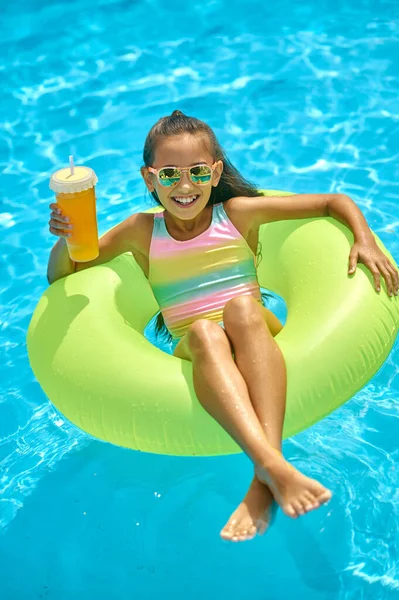 Girl on inflatable ring with drink looking at camera — Stock Photo, Image