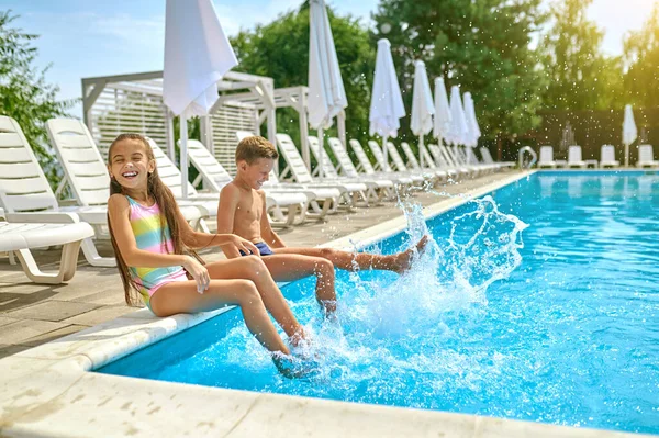 Crianças sentadas perto da piscina salpicando água — Fotografia de Stock