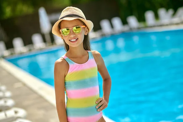 Дівчина в сонцезахисних окулярах посміхається на камеру біля басейну — стокове фото