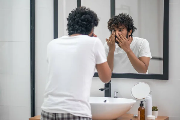 Concentrato giovane uomo esaminando la sua pelle del viso — Foto Stock