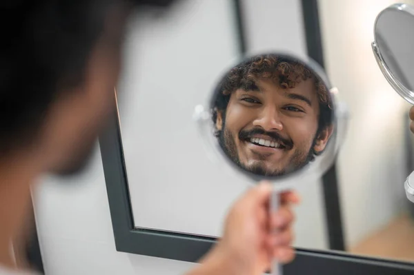 Alegre lindo macho sosteniendo el vidrio de mano antes de su cara — Foto de Stock