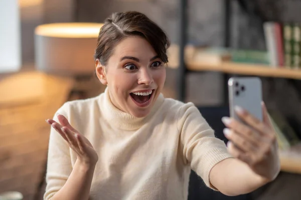 S otevřenou pusou gestikulující žena se dívá na svůj mobil — Stock fotografie
