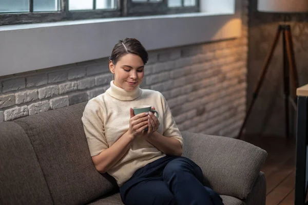 Serene lady with a beverage sitting on the sofa — Stock Photo, Image