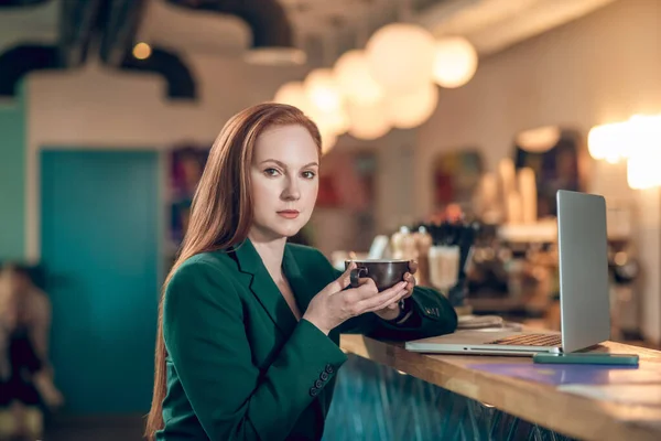 Mujer con café mirando a la cámara sentada en la cafetería —  Fotos de Stock