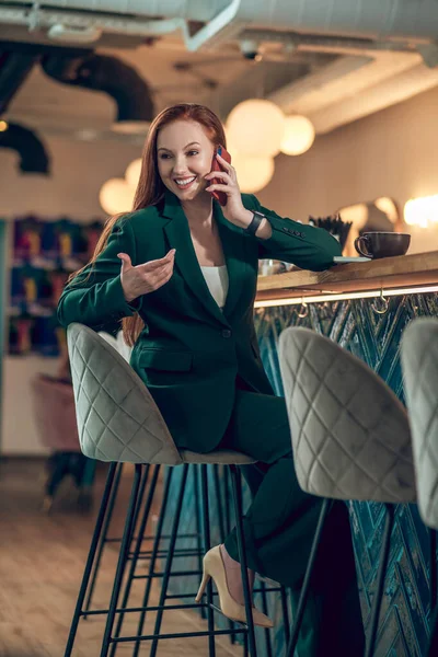 Mujer felizmente hablando en teléfono inteligente sentado en la cafetería — Foto de Stock