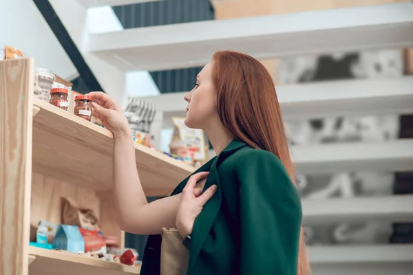 Frau betrachtet Glas mit Lebensmitteln im Ladenregal — Stockfoto
