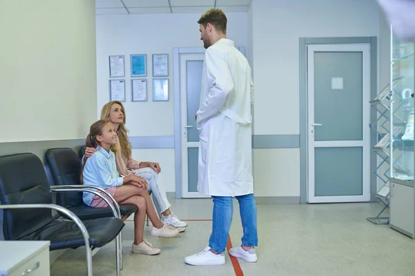 Νεαρός άνδρας γιατρός μιλάει στους ασθενείς στην αίθουσα της κλινικής — Φωτογραφία Αρχείου