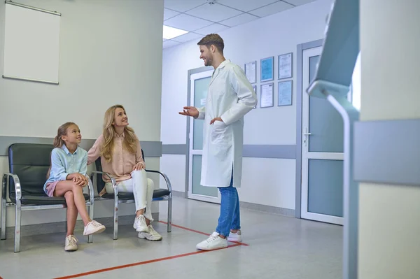 Νεαρός άνδρας γιατρός μιλάει στους ασθενείς στην αίθουσα της κλινικής — Φωτογραφία Αρχείου