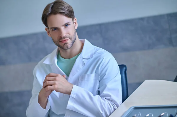 Молодий лікар в лабораторному пальто виглядає вдумливо — стокове фото