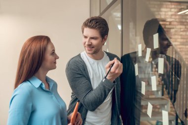 Duvarın yanında yapışkan notları olan bir adam kadına bakıyor.
