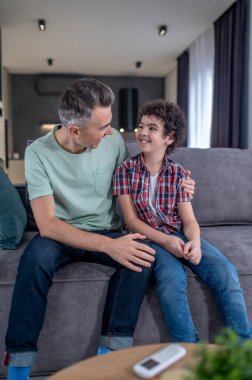 Adam evdeki kanepede oturan çocuğa sarılıyor.