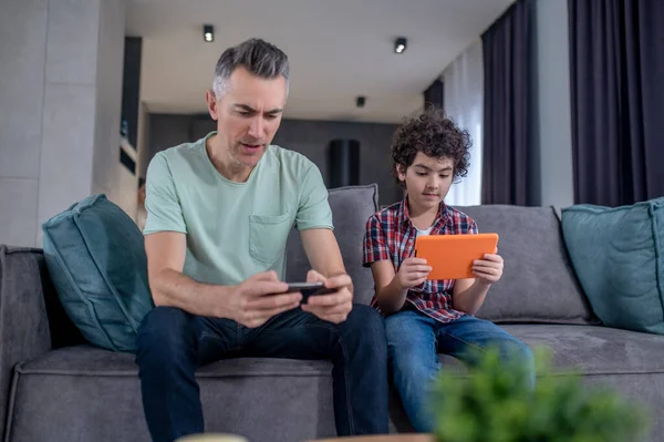 Hombre con smartphone niño con tableta sentado en el sofá — Foto de Stock