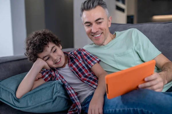 Hombre y niño mirando la tableta sentados en el sofá — Foto de Stock
