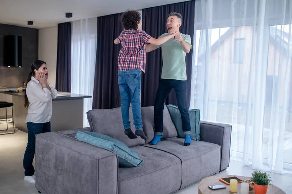 Man med pojke hoppar på soffan och överraskad kvinna — Stockfoto