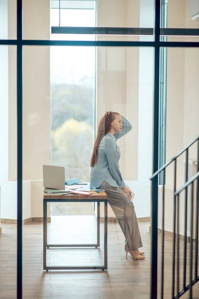 Tänkande kvinna lutar sig mot skrivbordet på kontoret — Stockfoto