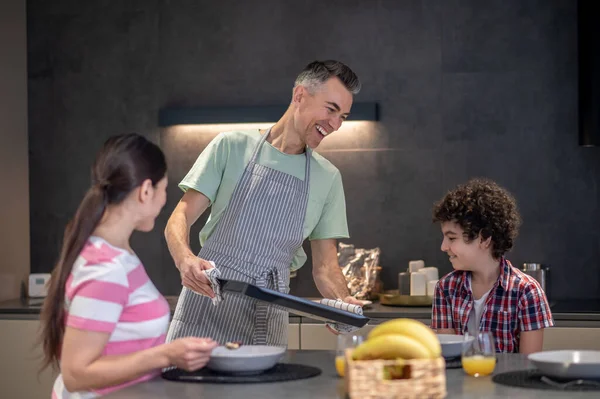 Oturan çocuğa ve kadına tava gösteren bir adam