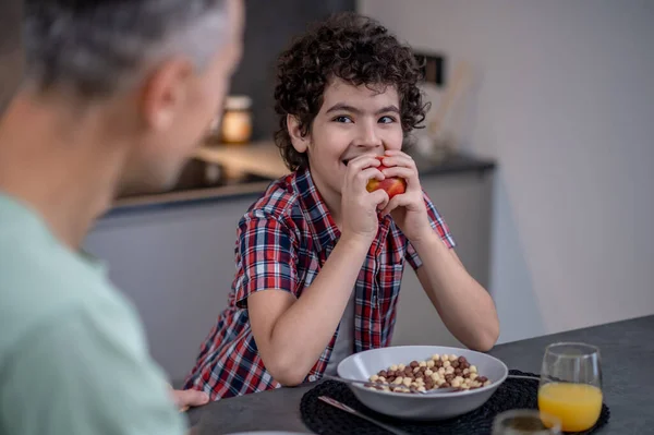 Junge isst Apfel und schaut Vater am Tisch an — Stockfoto