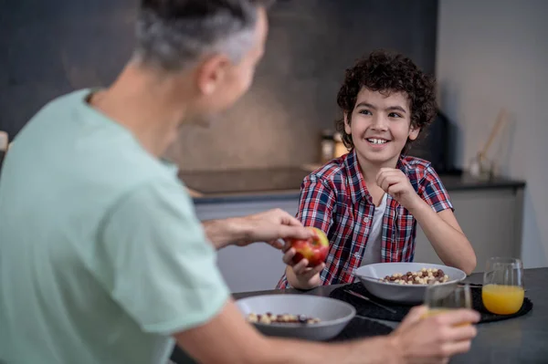 Niño tratando padre con manzana sentado en la mesa — Foto de Stock