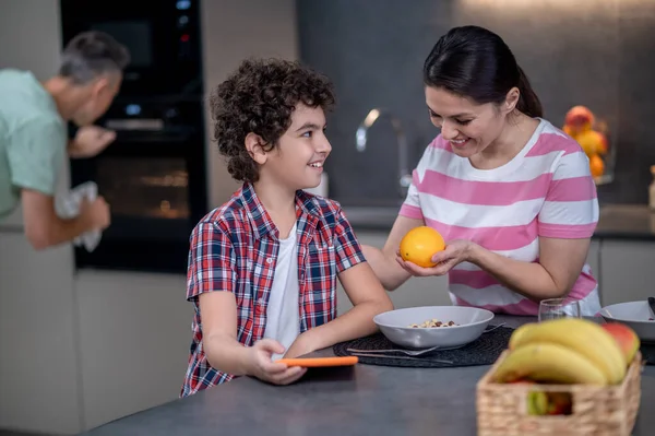 Narancsot ad a mosolygó fiúnak a konyhában. — Stock Fotó