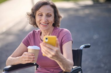 Elinde telefonu olan mutlu ve gülümseyen bir kadın.