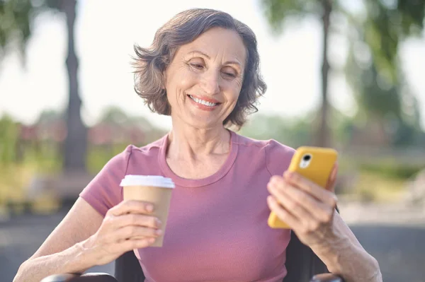 En kvinde med en telefon i hænderne ser glad og smilende ud - Stock-foto