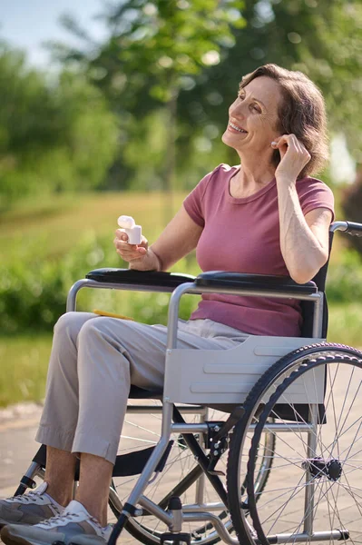 Une femme souriante sur un fauteuil roulant enfilant un casque sans fil — Photo