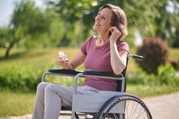 Une femme souriante sur un fauteuil roulant enfilant un casque sans fil — Photo