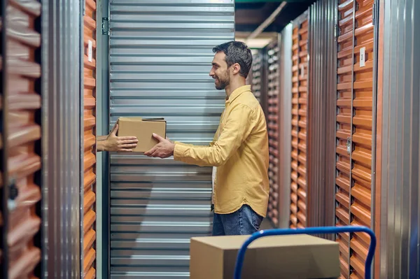 Usmívající se zaměstnanec skladu dává kartónovou krabici svému kolegovi — Stock fotografie