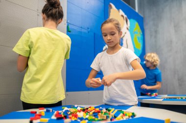 Lego parçaları tutan kız arkadaşlarıyla oynuyor.