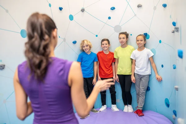 Los niños de la escuela de pie cerca de la pared mirando entrenador —  Fotos de Stock