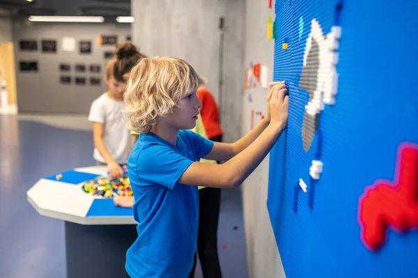 Προφίλ του αγοριού που συνδέει το κομμάτι lego με τον τοίχο — Φωτογραφία Αρχείου