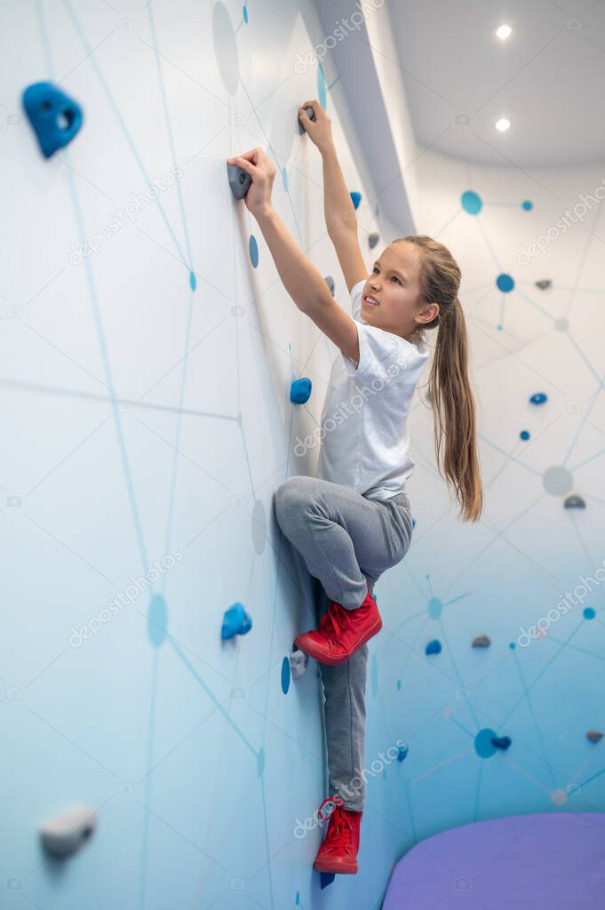 Girl climbing up wall sideways to camera