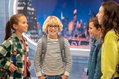 Çocuk kameraya bakıyor ve sınıf arkadaşlarıyla sohbet ediyor.