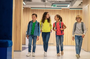 Sırt çantalı neşeli çocuklar koridorda yürüyor
