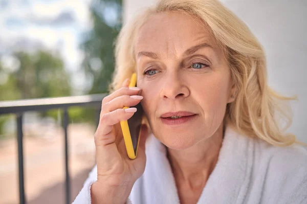 Egy szőke nő fehér köntösben telefonál. — Stock Fotó