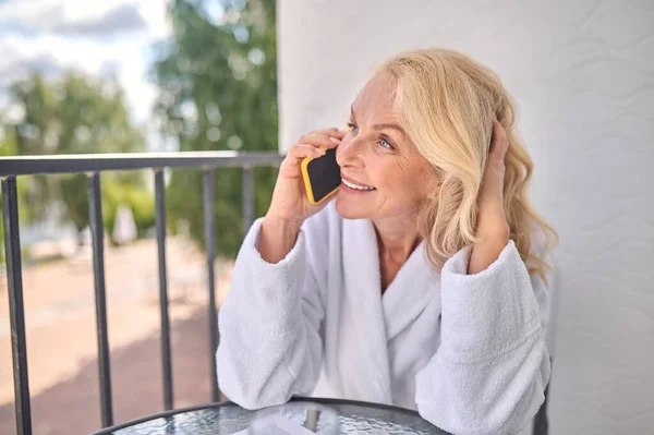 Blondynka w białym szlafroku rozmawiająca przez telefon — Zdjęcie stockowe