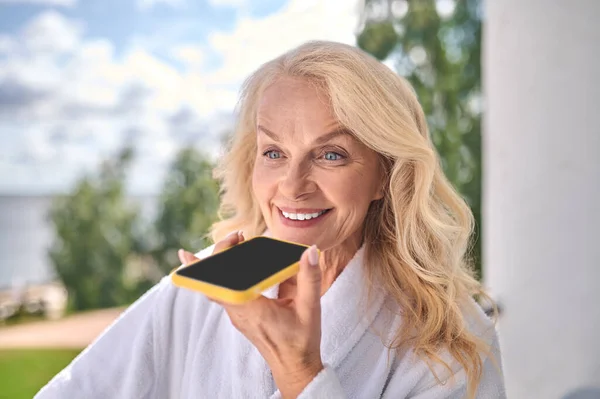 Une femme souriante en robe blanche avec un smartphone dans les mains — Photo