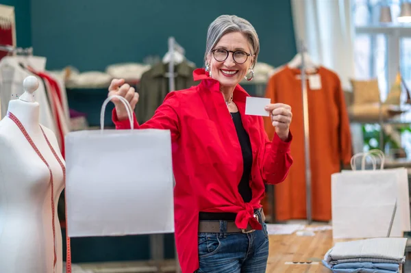 Mujer mostrando paquete y tarjeta a la cámara — Foto de Stock