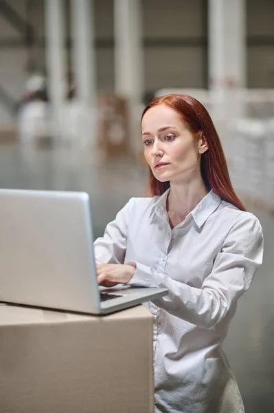Mulher trabalhando no laptop no armazém industrial — Fotografia de Stock