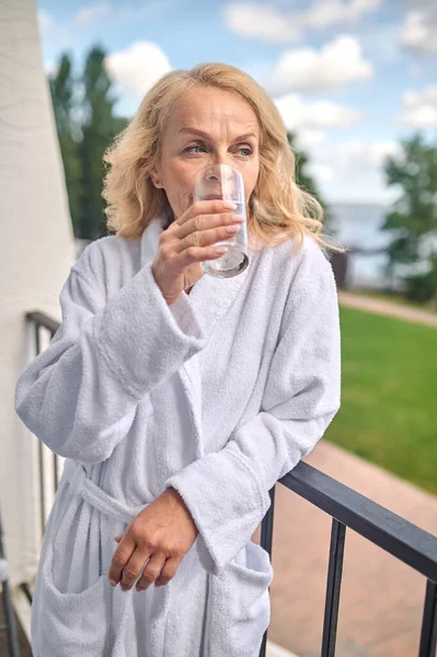 Блондинка в білому халаті зі склянкою води — стокове фото