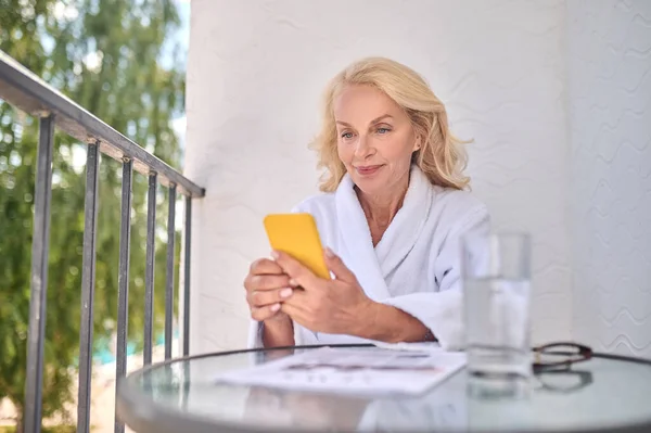 Elinde akıllı telefon olan beyaz cüppeli sarışın bir kadın. — Stok fotoğraf