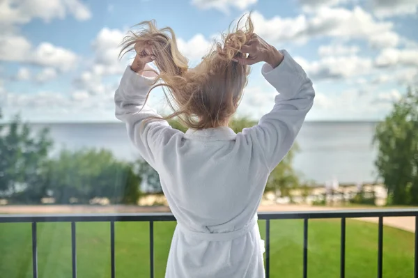 En blond kvinna i vit morgonrock står på balkongen — Stockfoto